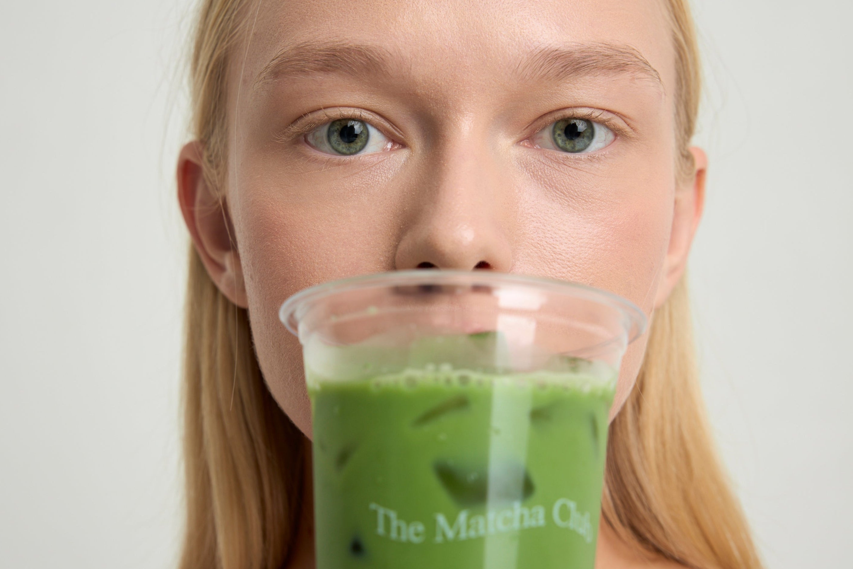 Person holding a glass of green matcha drink with 'The Matcha Club' branding.